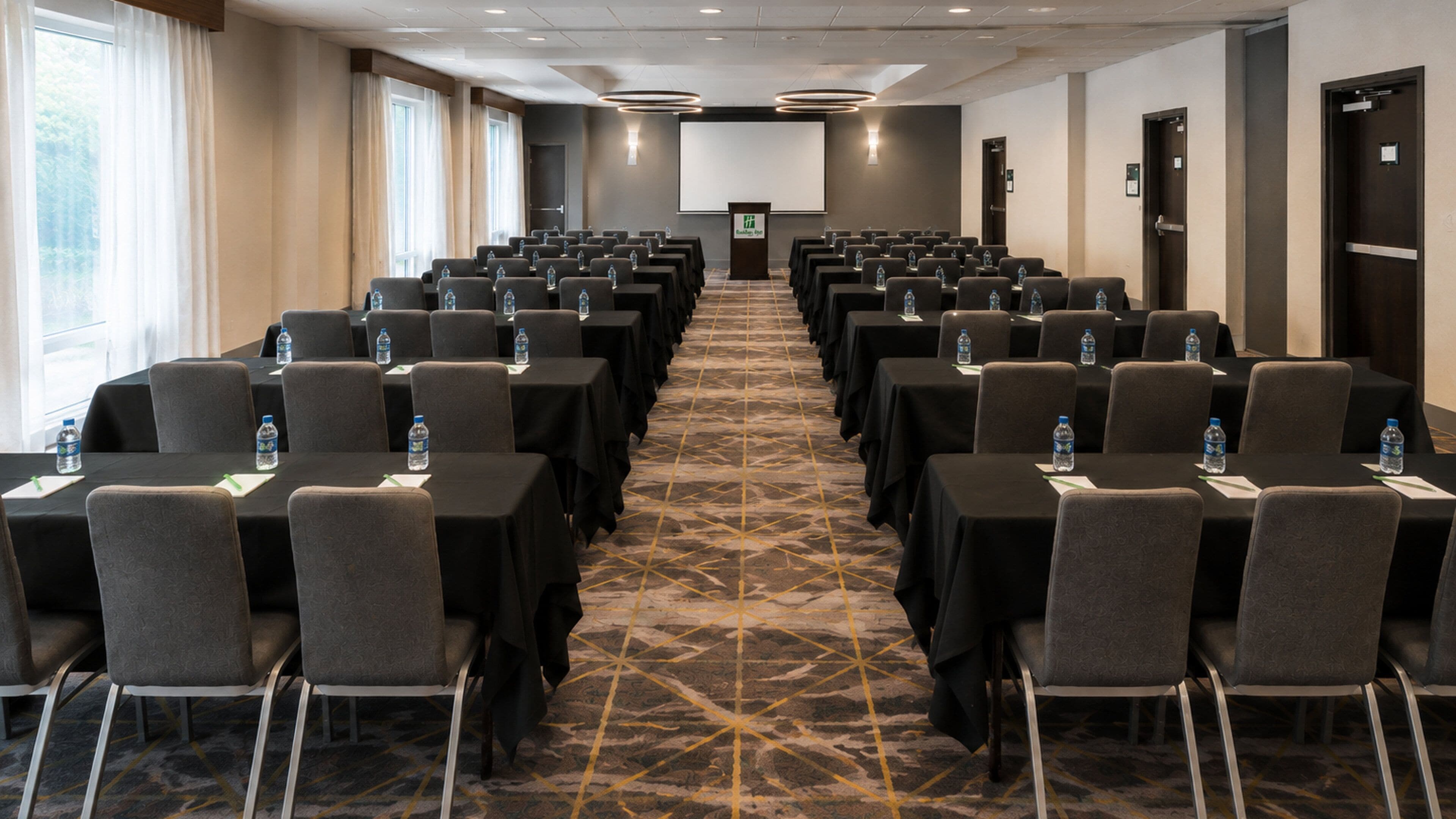 A conference room with rows of tables and chairs, a podium, and a projector screen.