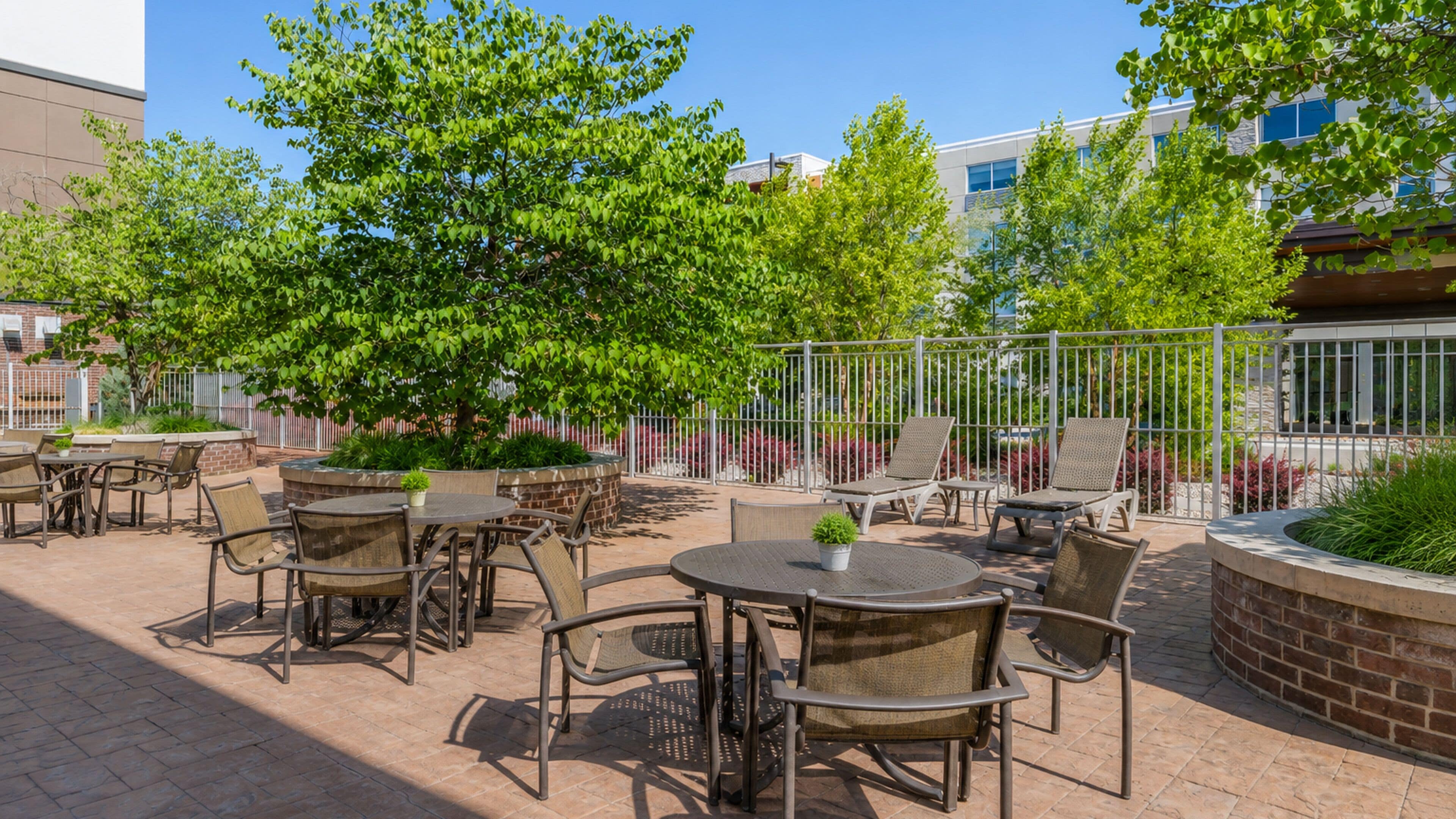 An outdoor patio area with round tables and chairs, surrounded by a brick wall and metal fencing.