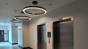 Corredor moderno com três elevadores, uma placa indicando uso dos elevadores em emergências e piso revestido de azulejos.