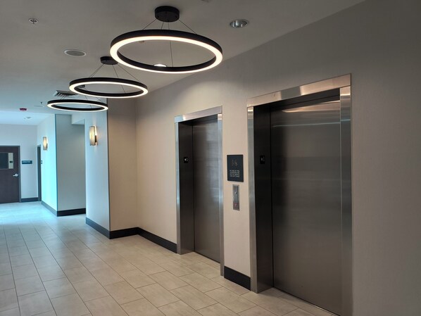 A modern hallway with three elevators, a sign indicating elevator use for emergencies, and a clean, tiled floor. - Holiday Inn Boise Airport by IHG (Boise)