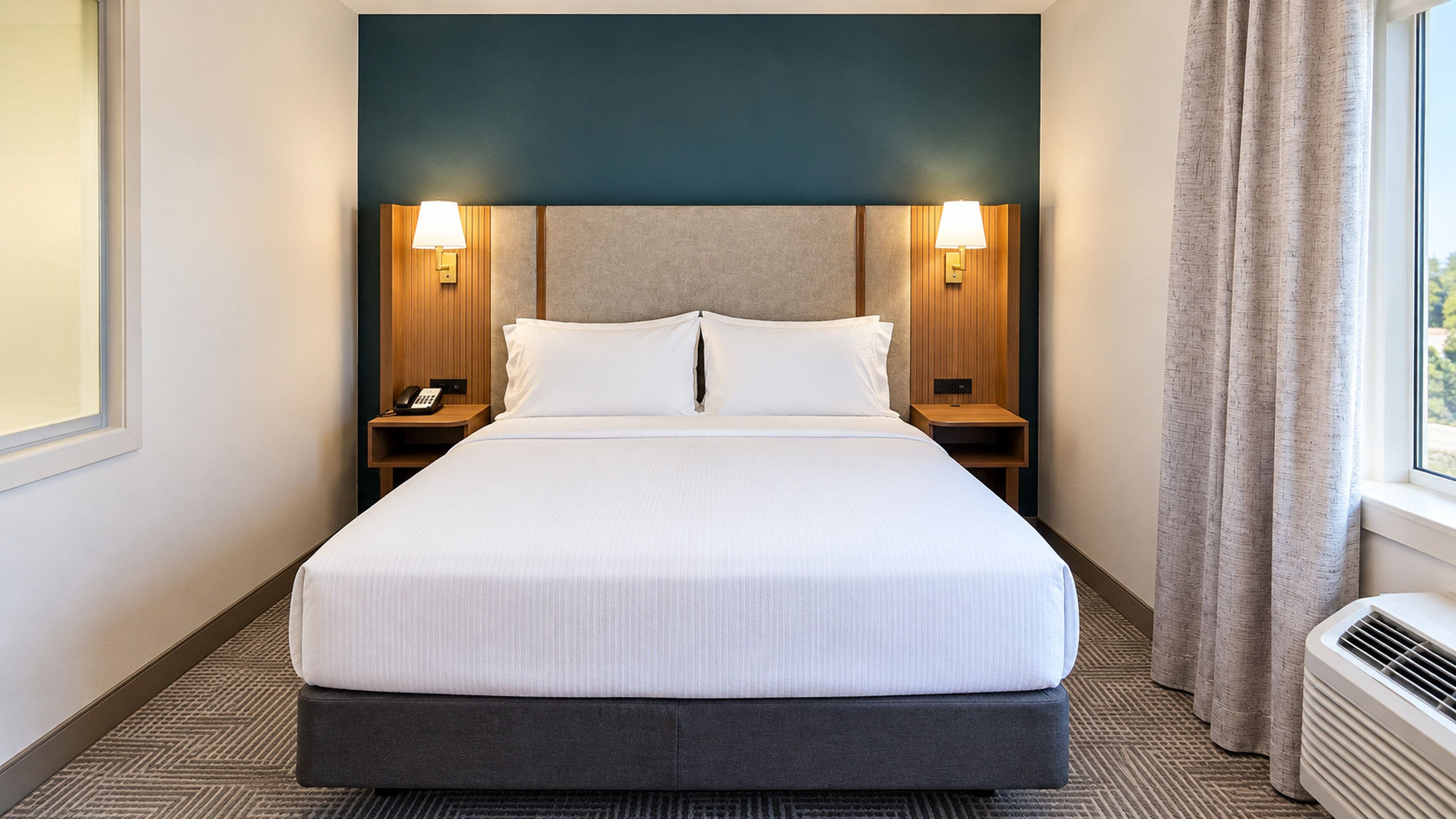 A hotel room with a large bed, two bedside lamps, a telephone, and a window with curtains.