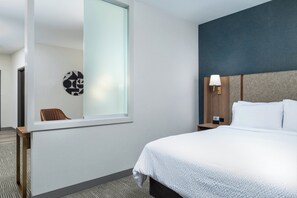 A hotel room with a large bed, a nightstand, a wall-mounted lamp, and a window with a view of another room. - Holiday Inn Boise Airport by IHG (Boise)