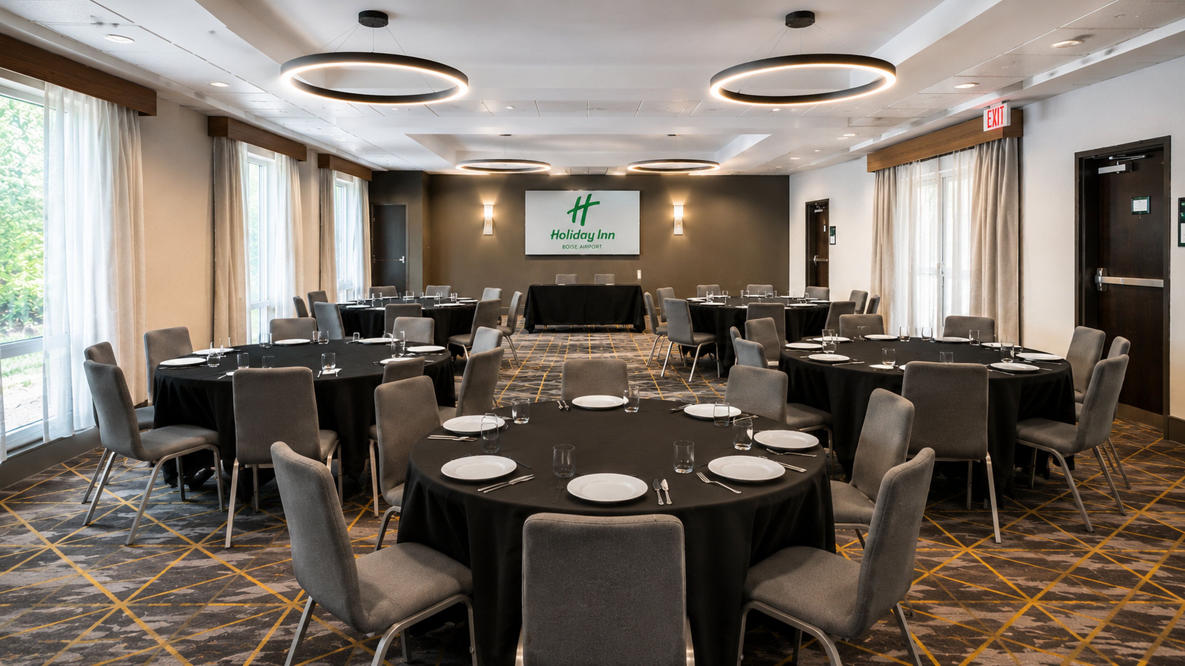 A conference room with round tables, chairs, and a large screen at the front.