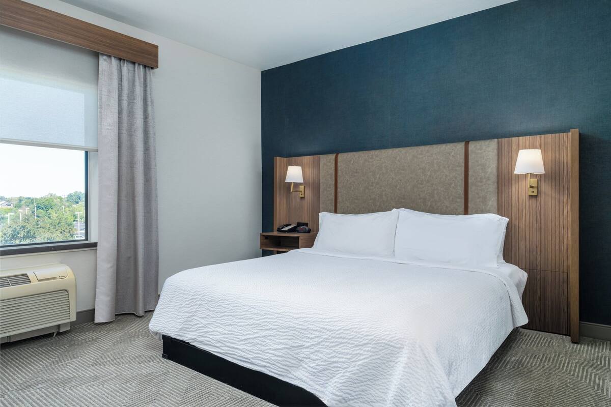 Une chambre d’hôtel avec un grand lit, une table de chevet, une lampe et une vue sur l’extérieur.