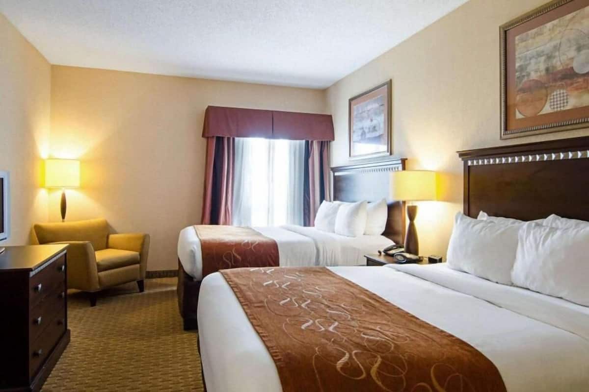 A hotel room with two beds, a desk, a chair, and a TV.