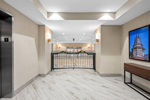 A hotel corridor with a marble floor, a staircase, a wall-mounted TV, and a gate with greenery.