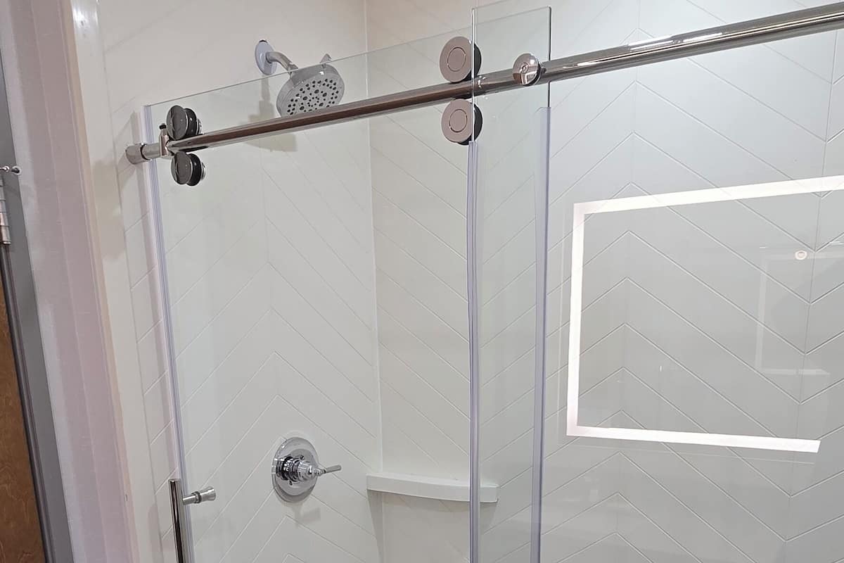 A glass-enclosed shower area with a control panel and a ventilation grate.