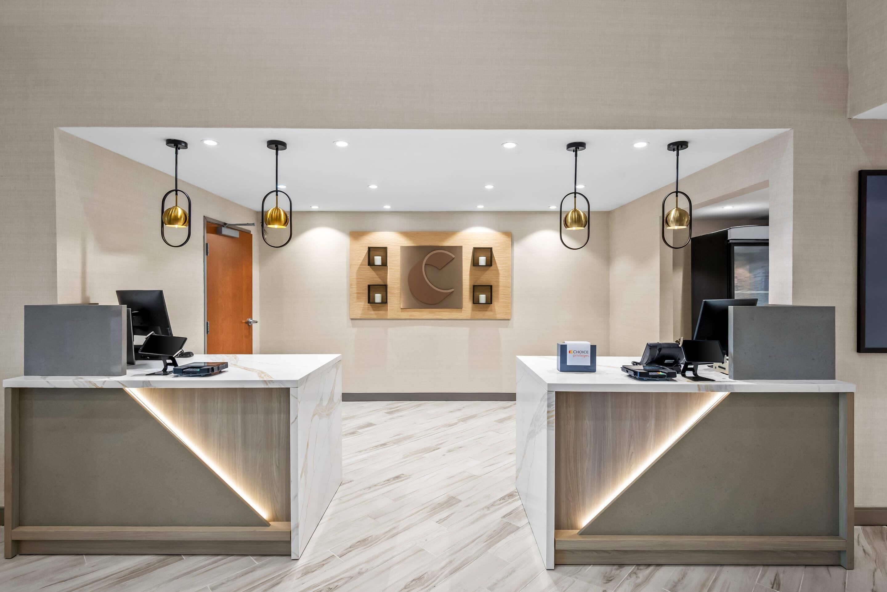 A reception area with two reception desks, modern pendant lighting, a wooden accent wall, and a tiled floor.