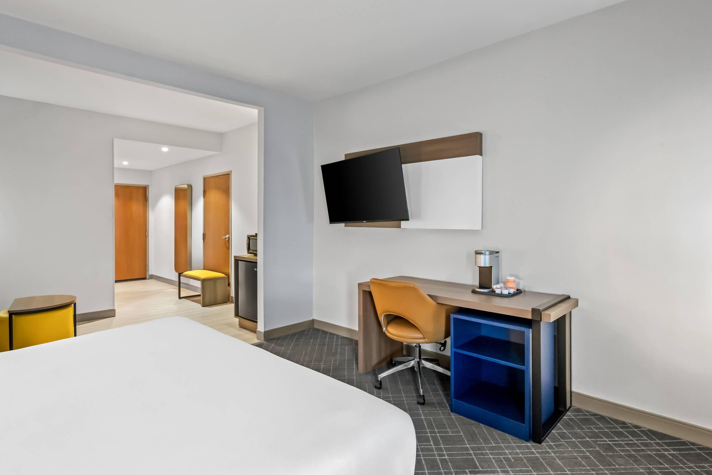Une chambre d’hôtel équipée d’un lit, d’un bureau avec une chaise, d’un téléviseur fixé au mur et d’une machine à café.