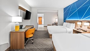 Een hotelkamer met een bureau, twee bedden, een televisie en een groot blauw kunstwerk aan de muur.