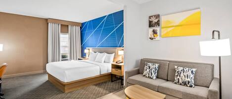 Una habitación de hotel con cama, sofá, una mesita y obras de arte en la pared.