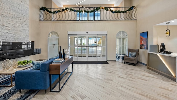 Een ruime lobby met een modern design, inclusief een zithoek met een blauwe bank en een houten tafel, een receptiebalie en uitzicht op buiten via grote glazen deuren.