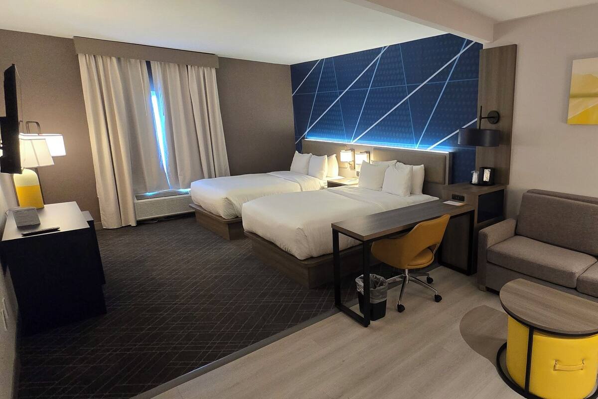 A hotel room with two beds, a desk, a sofa, a small table, and a trash bin.