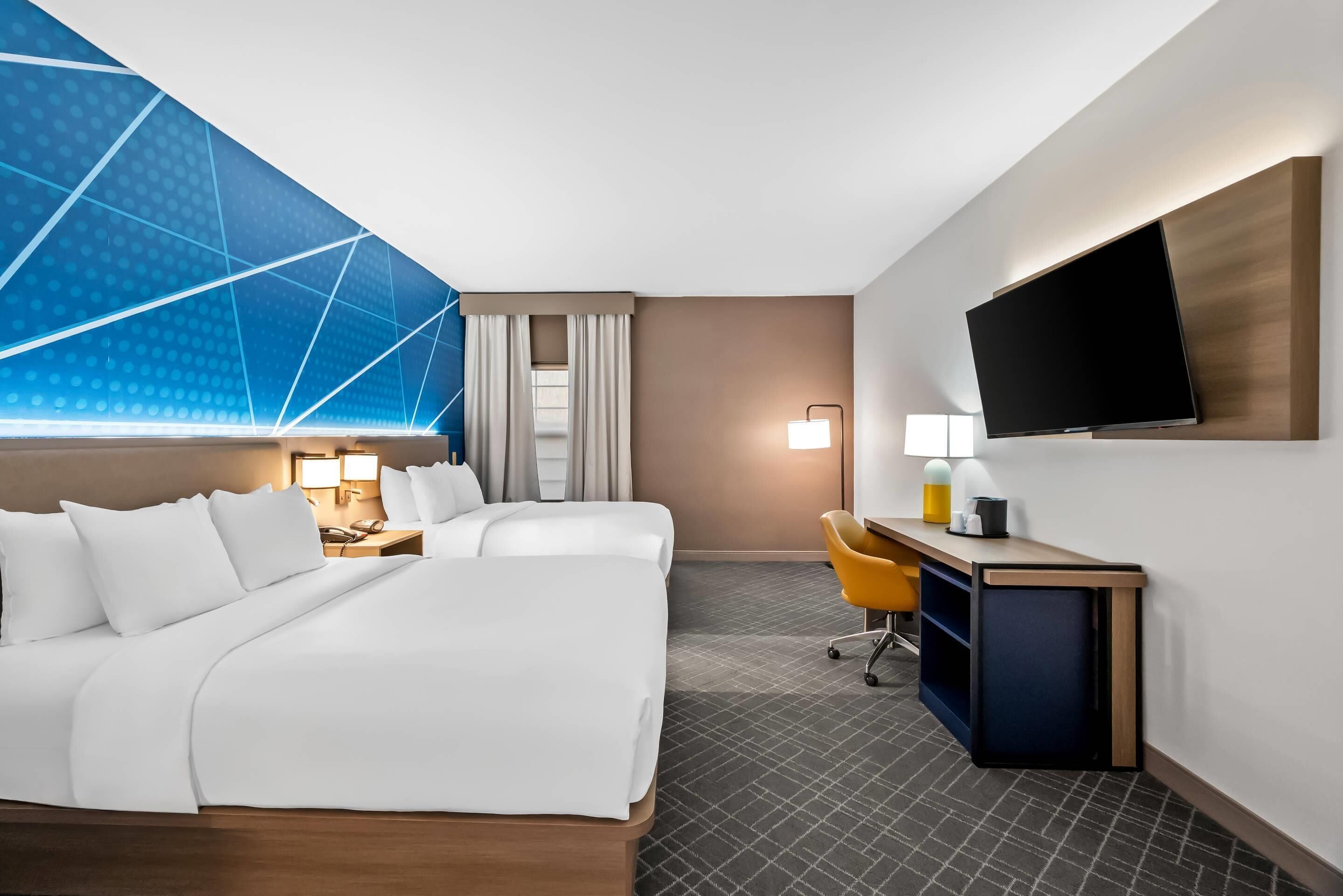 A hotel room with a bed, a desk, a chair, a TV, and a window with curtains.