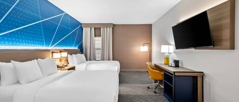 A hotel room with a bed, a desk, a chair, a TV, and a window with curtains.