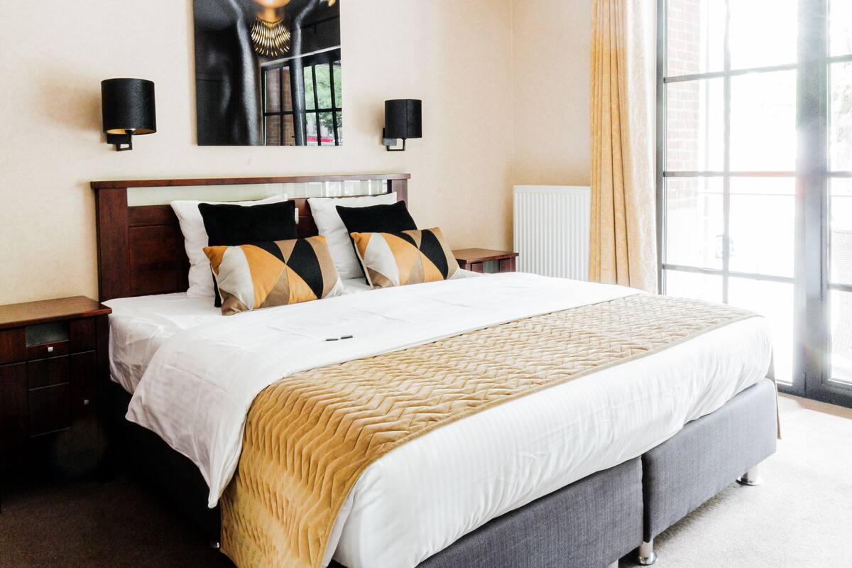 Une chambre d’hôtel moderne avec un grand lit, un tableau au mur et une vue par la fenêtre.