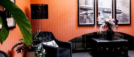 A room with a black armchair, a side table with a vase of flowers, a floor lamp, and three framed pictures on the wall.