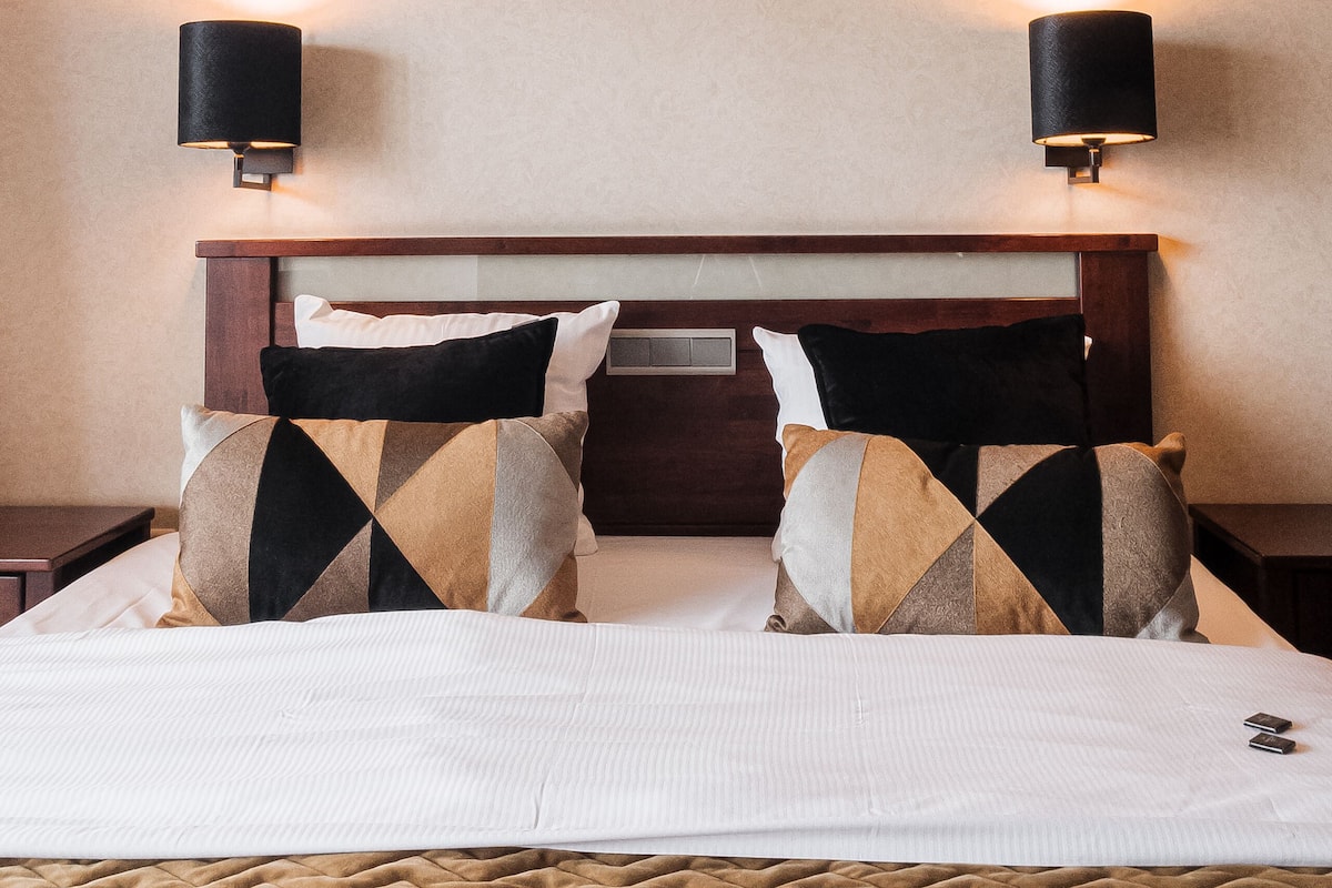 Une chambre d’hôtel avec un lit, deux oreillers, une tête de lit et deux lampes fixées au mur.