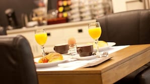 A breakfast table with orange juice, a coffee cup, and a plate of food. There are chairs around the table, and a lamp is on the wall. - Turnhout City Hotel (Turnhout)