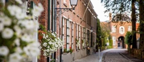 Une rue pavée bordée d’immeubles en briques, dont certains sont ornés de jardinières fleuries.