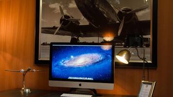Een bureau met een computer beeldscherm waarop een afbeelding van een sterrenstelsel staat, een afbeelding van een vliegtuig in een lijst en een bureaulamp.