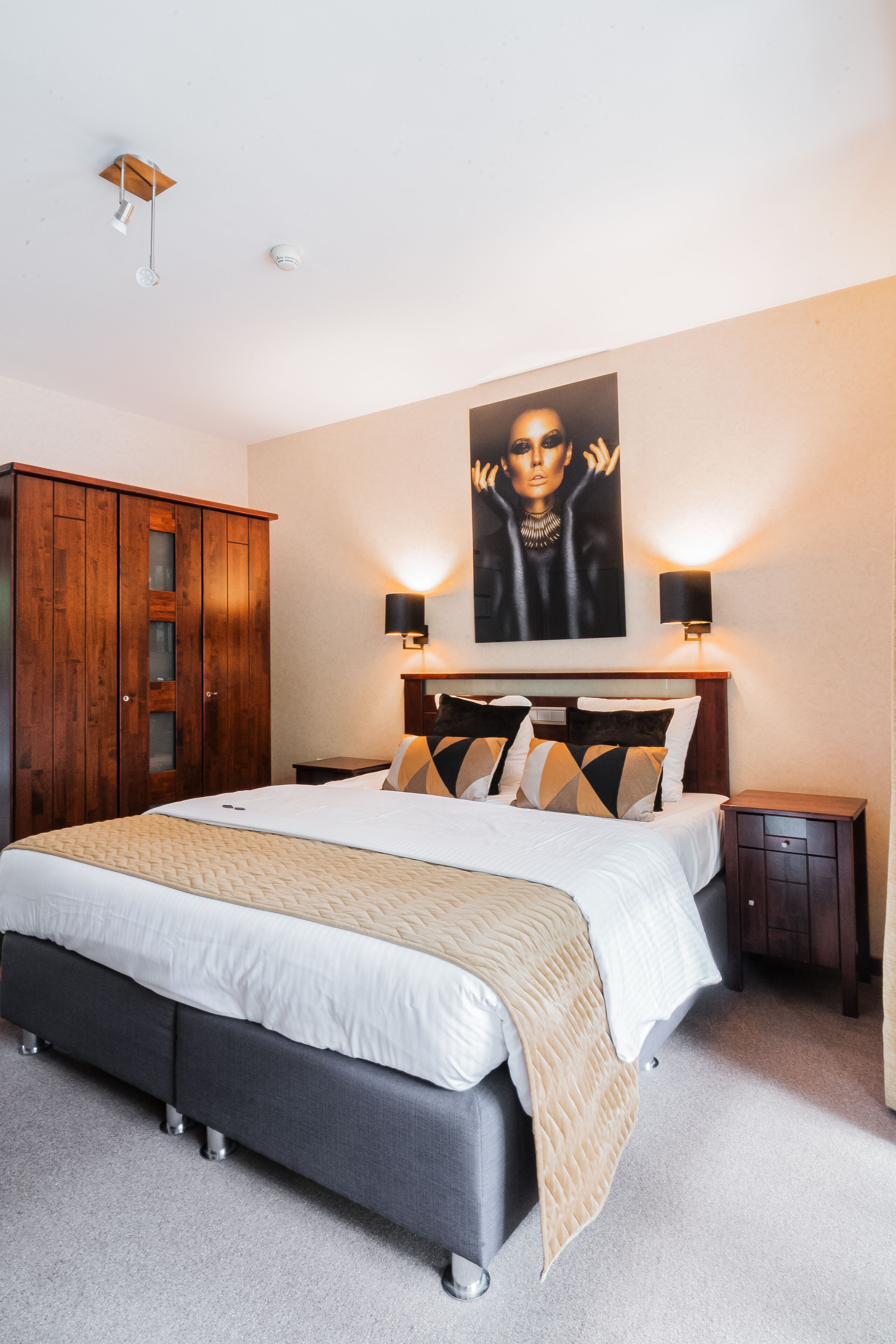 A bedroom with a large bed, wooden wardrobe, and a painting on the wall.