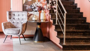 A staircase with a metal railing, a framed artwork above it, and a chair with a vase of flowers beside it. - Turnhout City Hotel (Turnhout)