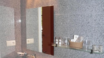 A bathroom with a granite wall, a white sink, a mirror, and a shelf with toiletries.