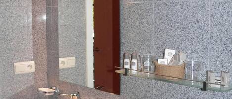Une salle de bain avec un mur en granit, un lavabo blanc, un miroir et une étagère contenant des articles de toilette.
