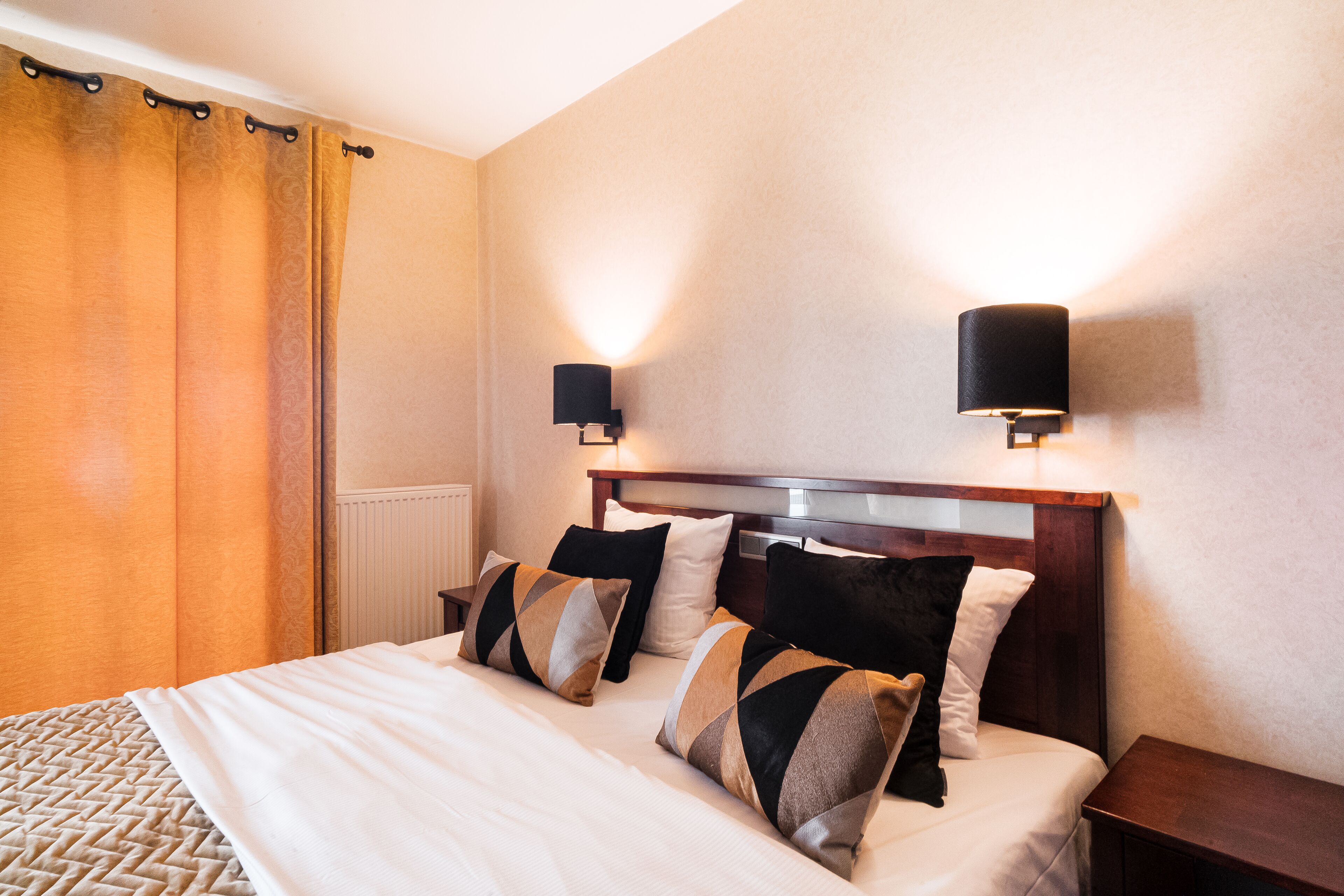 A neatly made bed with a patterned bedspread, two wall-mounted lamps, and a wooden nightstand.