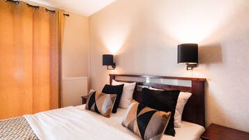 A neatly made bed with a patterned bedspread, two wall-mounted lamps, and a wooden nightstand.