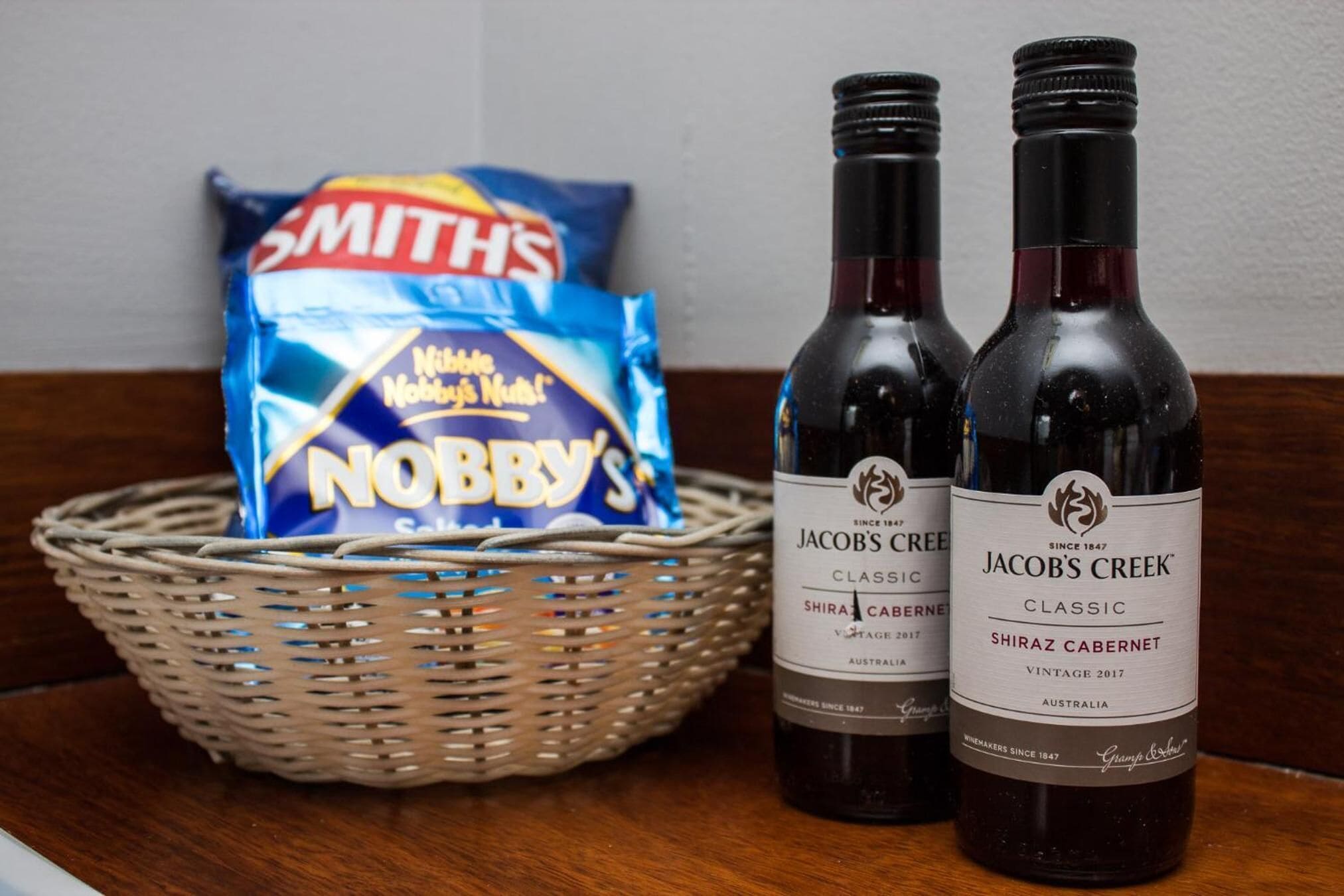 Dos botellas de Jacob's Creek Classic Shiraz Cabernet y una cesta con una bolsa de chips Smith's Nobby's.