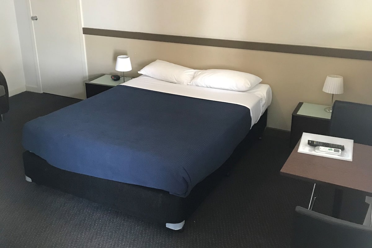 A hotel room with a bed, a nightstand, a desk, and a chair.