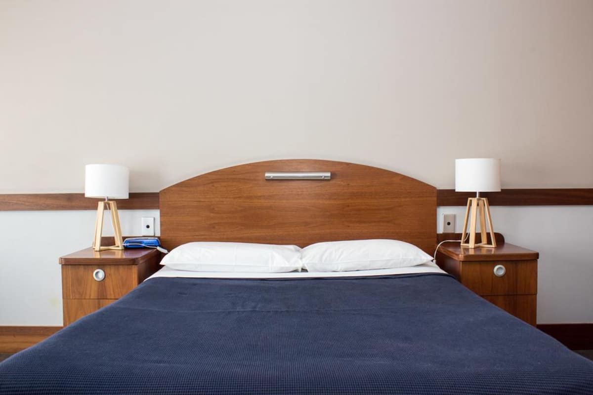 A neatly made bed with a dark blue bedspread, two bedside tables with lamps, and a wooden headboard.