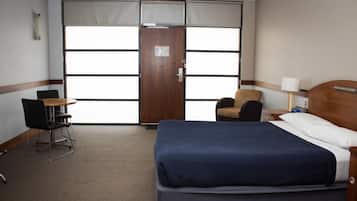 Hotellihuone, jossa on suuri sänky, tuoli, työpöytä ja ikkuna, jossa on sälekaihtimet.