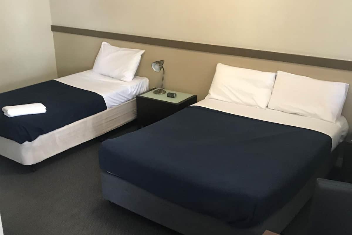 A hotel room with two single beds, each with a white pillow and a dark blue bedspread. There is a nightstand with a lamp and a phone between the beds.