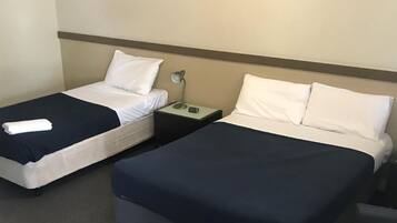 Habitación de hotel con dos camas individuales, cada una con almohada blanca y colcha azul oscuro. Entre las camas, una mesita de noche con lámpara y teléfono.