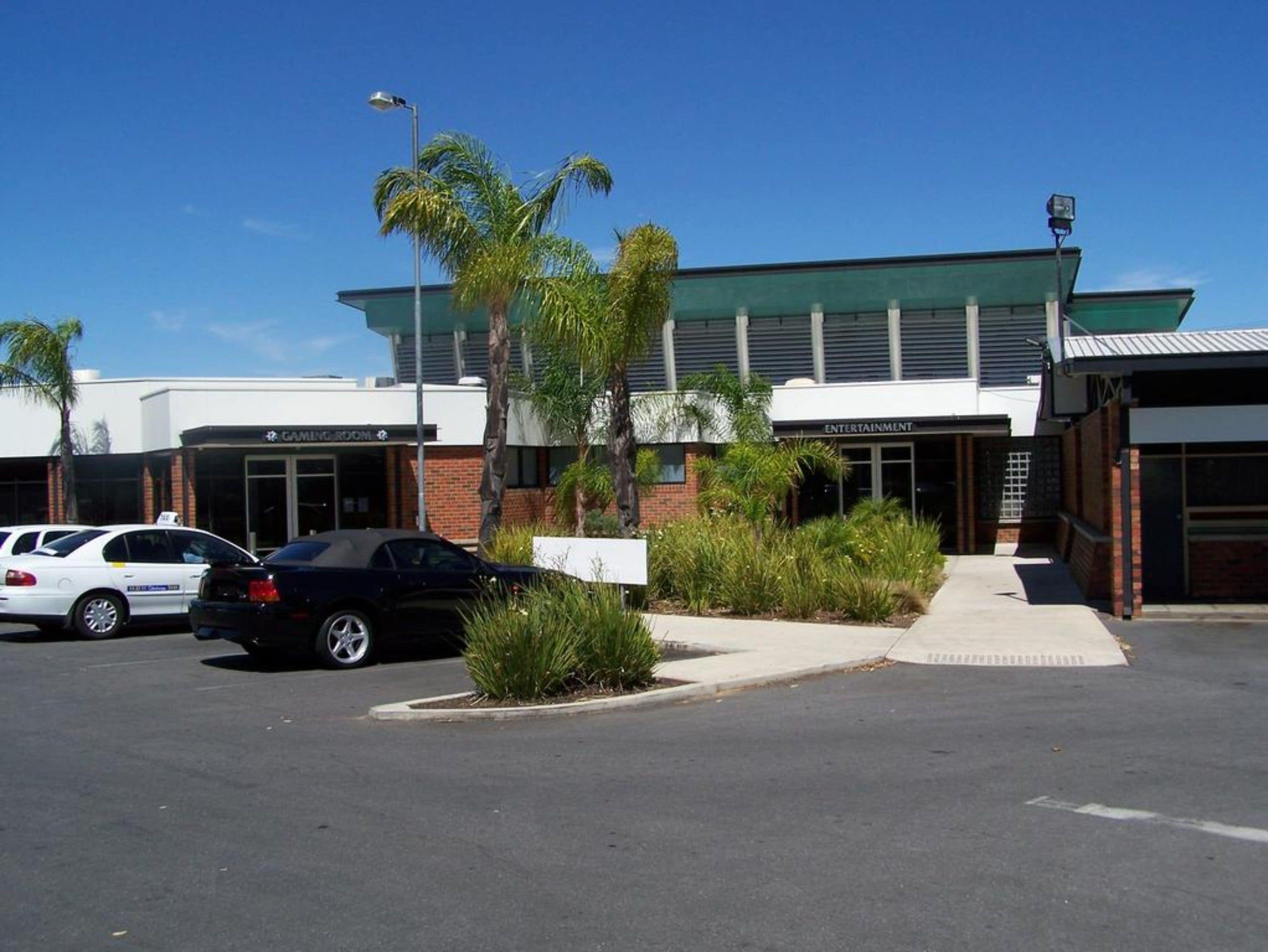 A building with a green roof, a gaming room, and an entertainment area. There are cars parked in front.