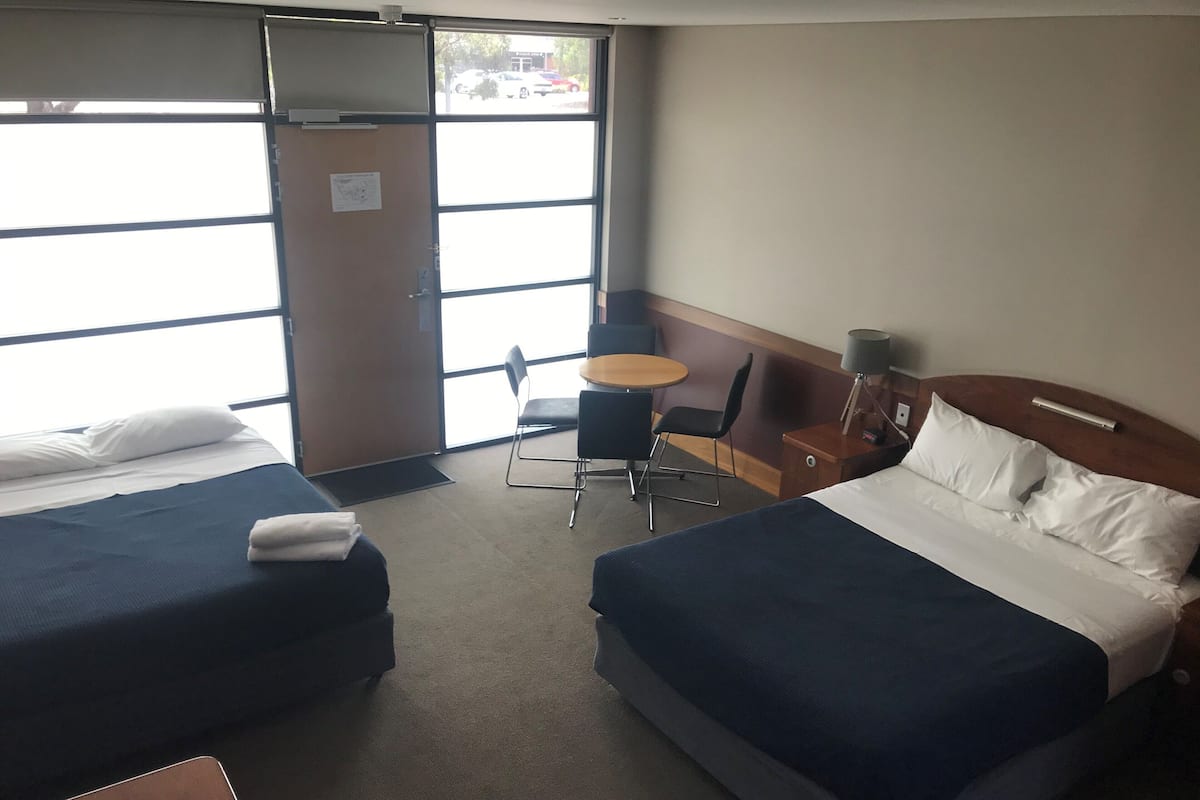 A hotel room with two beds, a desk, a chair, and a small table.