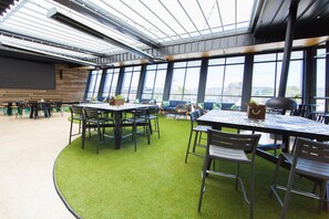 An indoor dining area with tables and chairs, large windows, and a view of the outdoors. - Highlander Hotel (Gilles Plains)