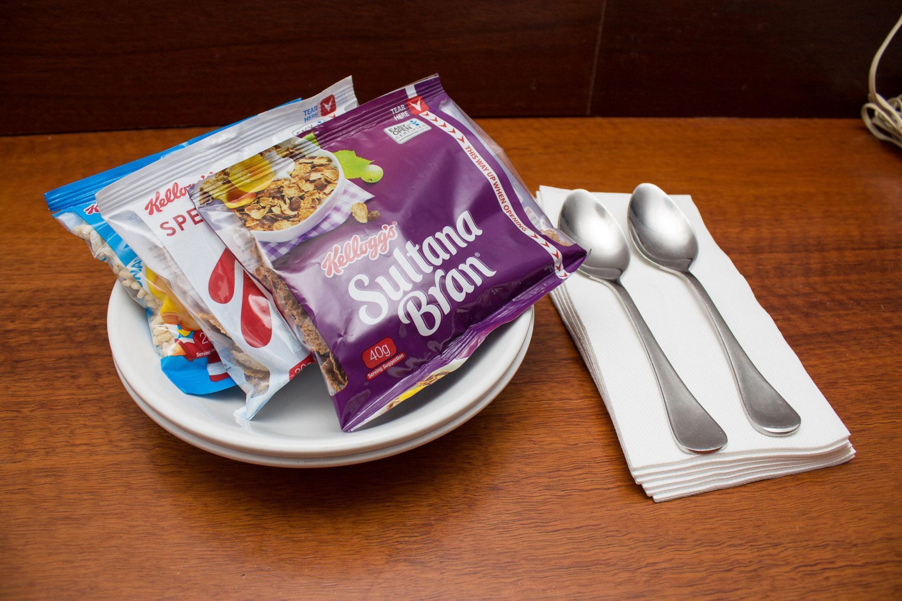 Een bord met twee pakken Kellogg’s Sultana Bran en een lepel op een houten tafel.
