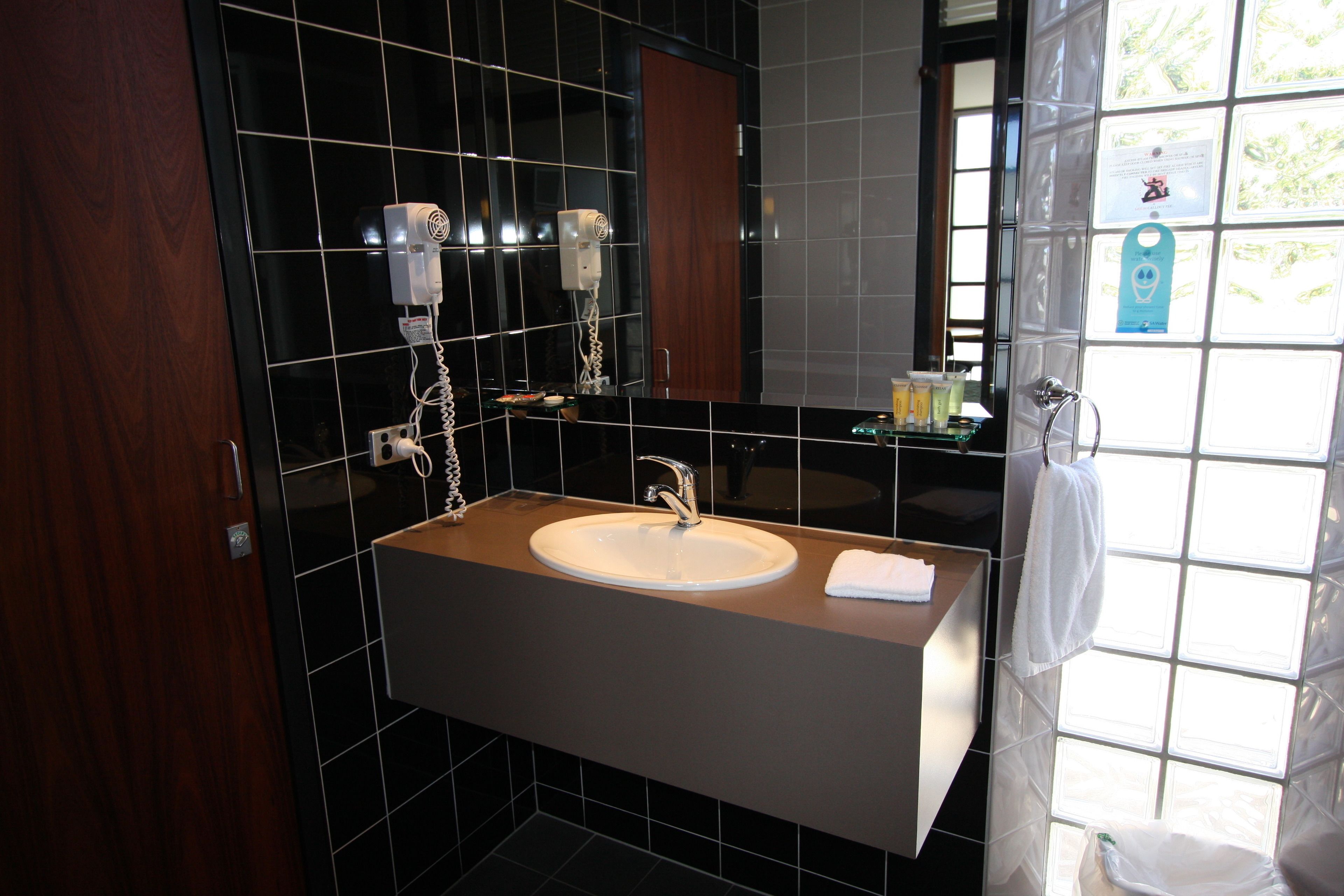 Un baño moderno con un lavamanos grande, un espejo y dos secadores de pelo fijados a la pared.