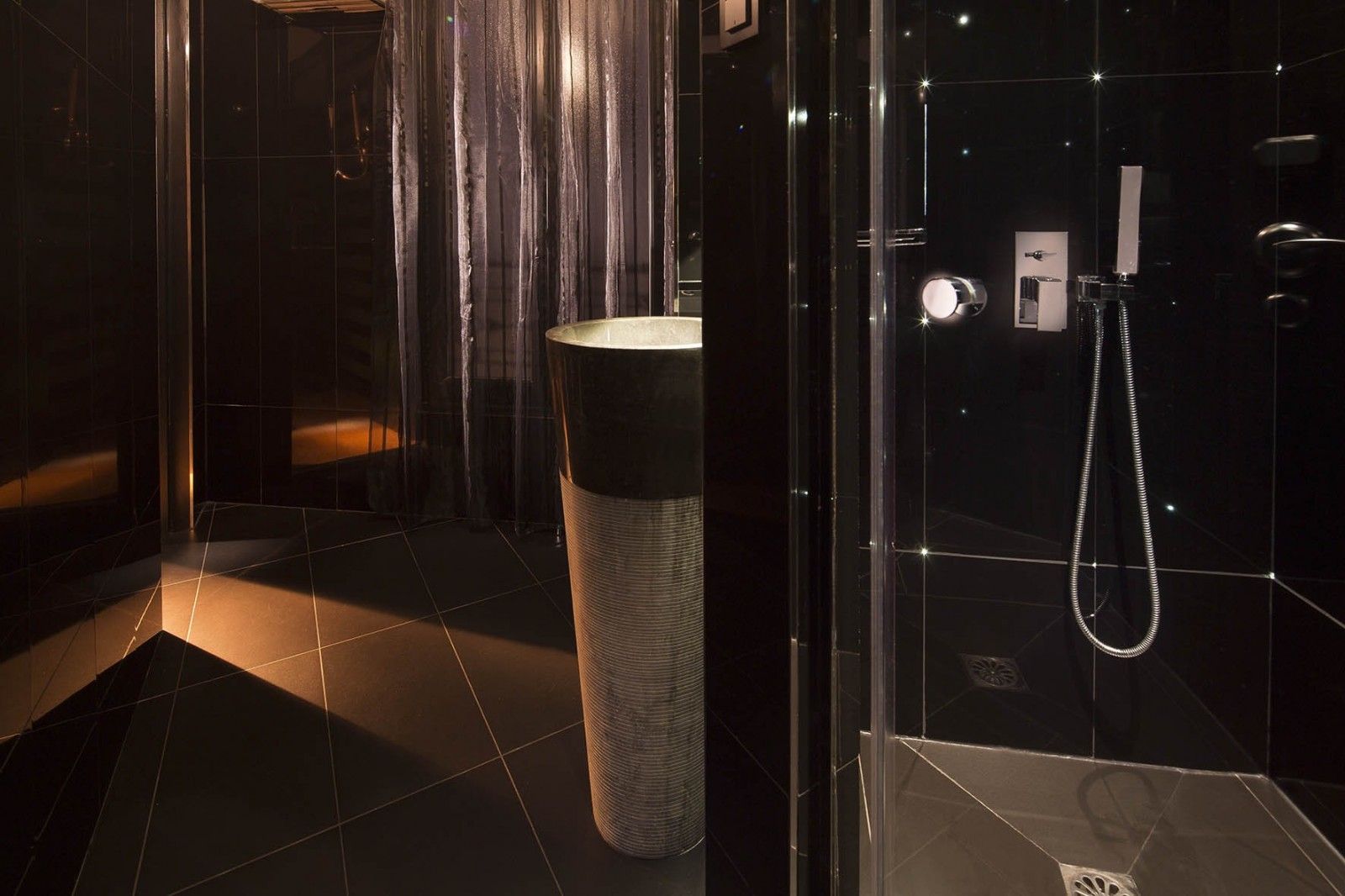 A modern bathroom with a glass shower enclosure, a tall cylindrical sink, and a wall-mounted faucet.