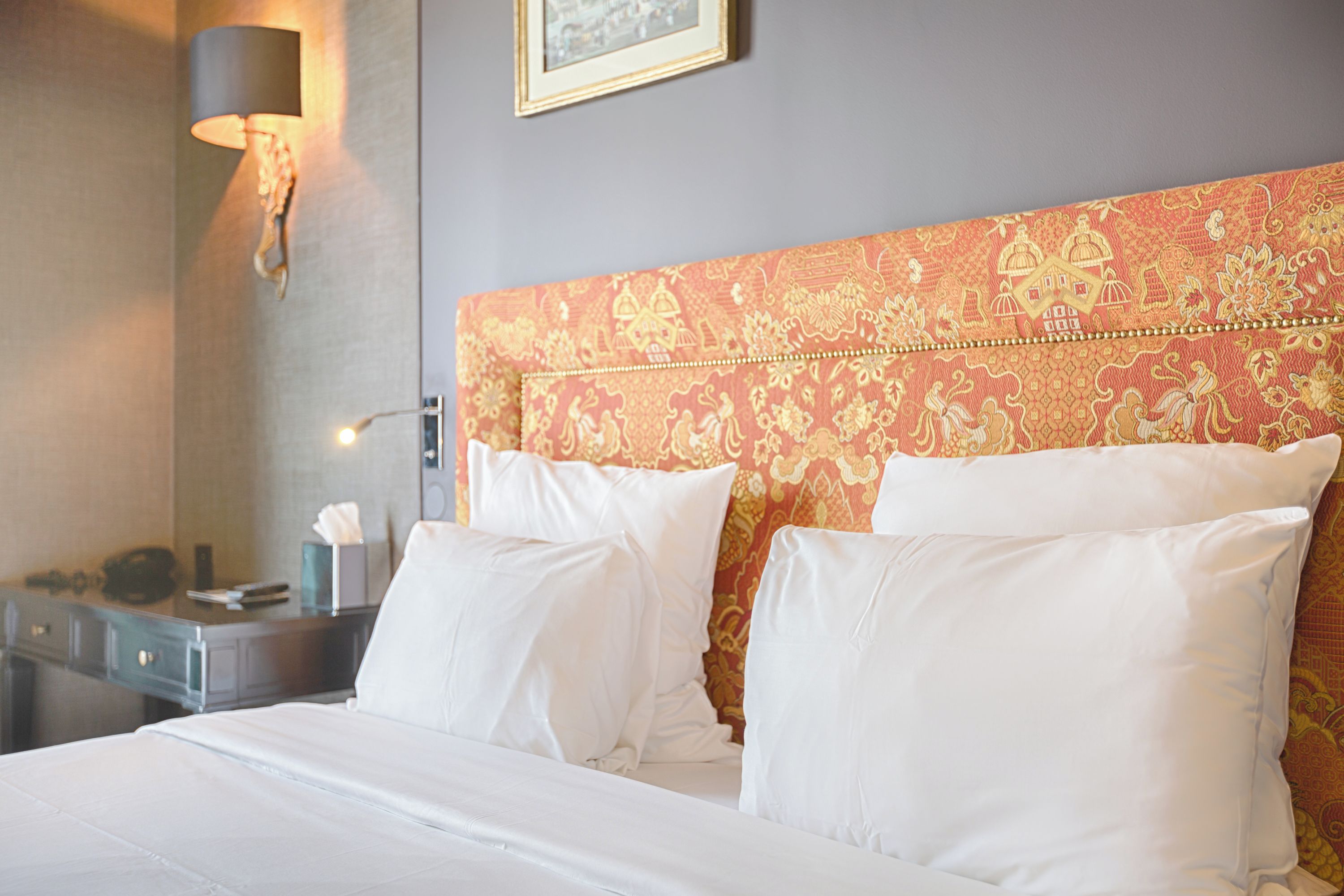 Habitación de hotel con cama, almohadas blancas, mesita de noche, lámpara y un diseño decorativo en la pared.