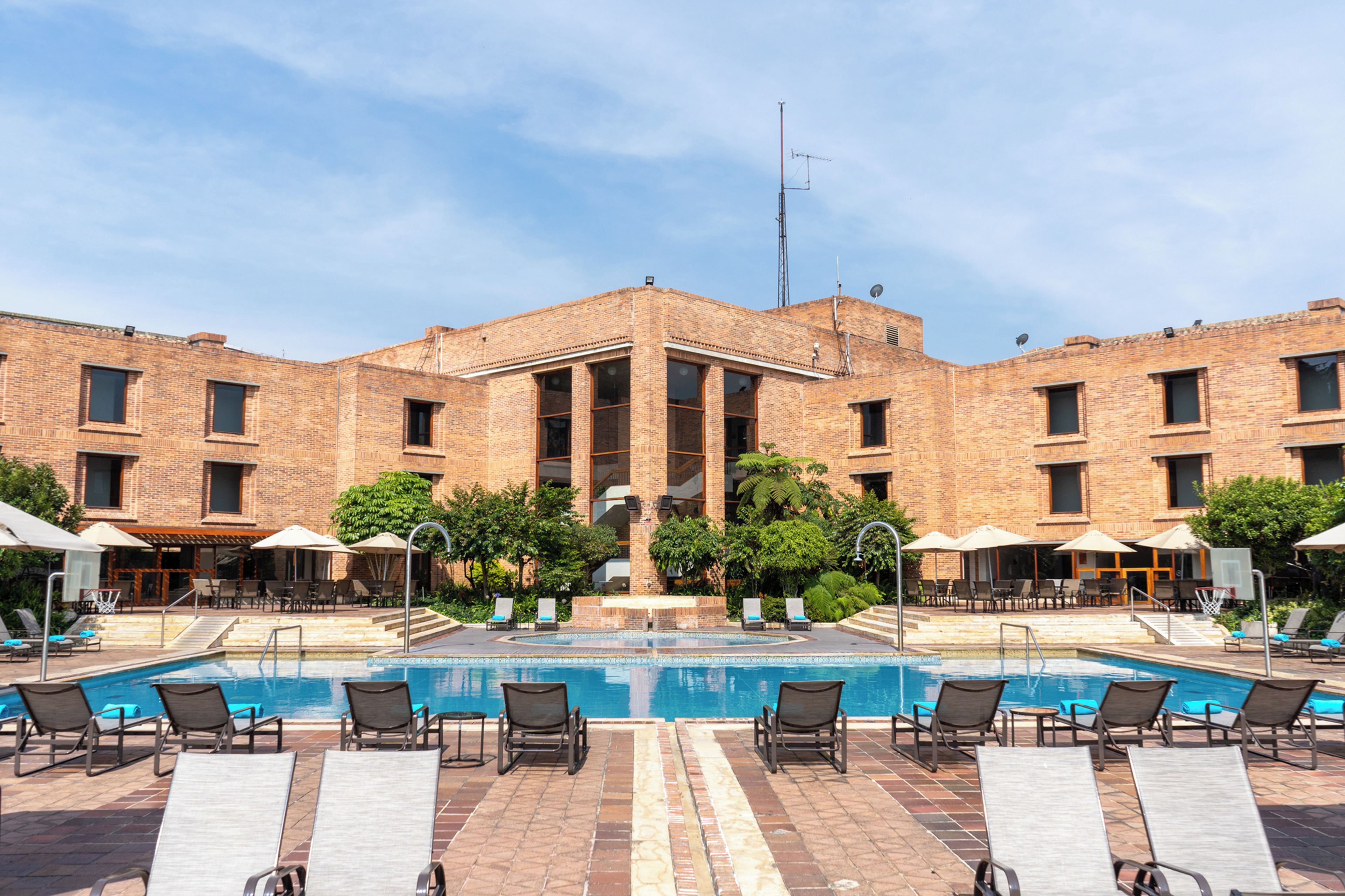 A hotel with a swimming pool, lounge chairs, and a brick facade.