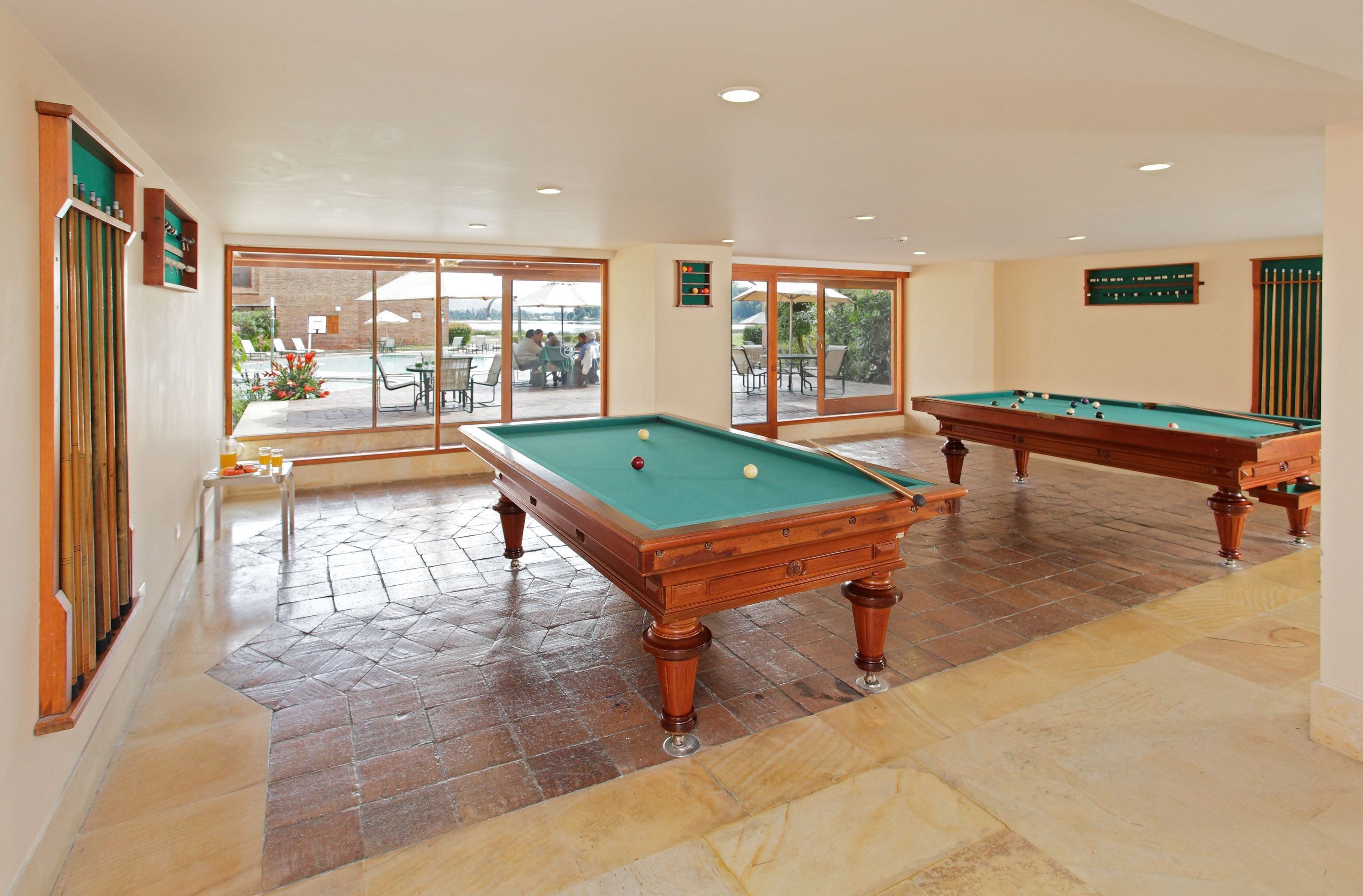 A pool table in a well-lit indoor area with large windows and a view of an outdoor patio.