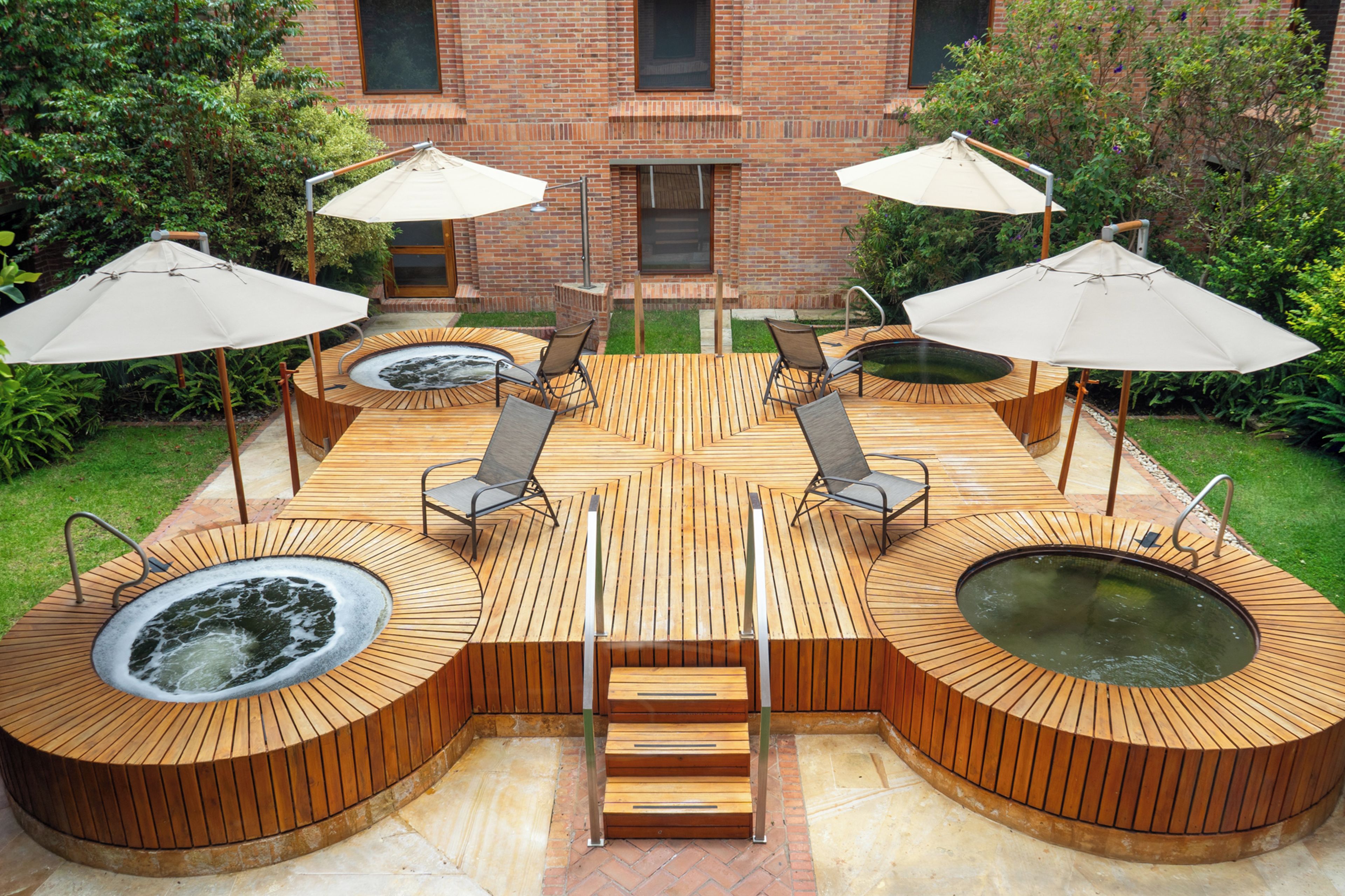 Una terraza de madera con dos jacuzzis, un pozo de fuego y asientos de exterior con sombrillas.