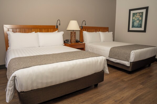 Ein Hotelzimmer mit zwei Betten, einem Nachttisch mit Lampe, einem gerahmten Bild an der Wand und Holzboden.