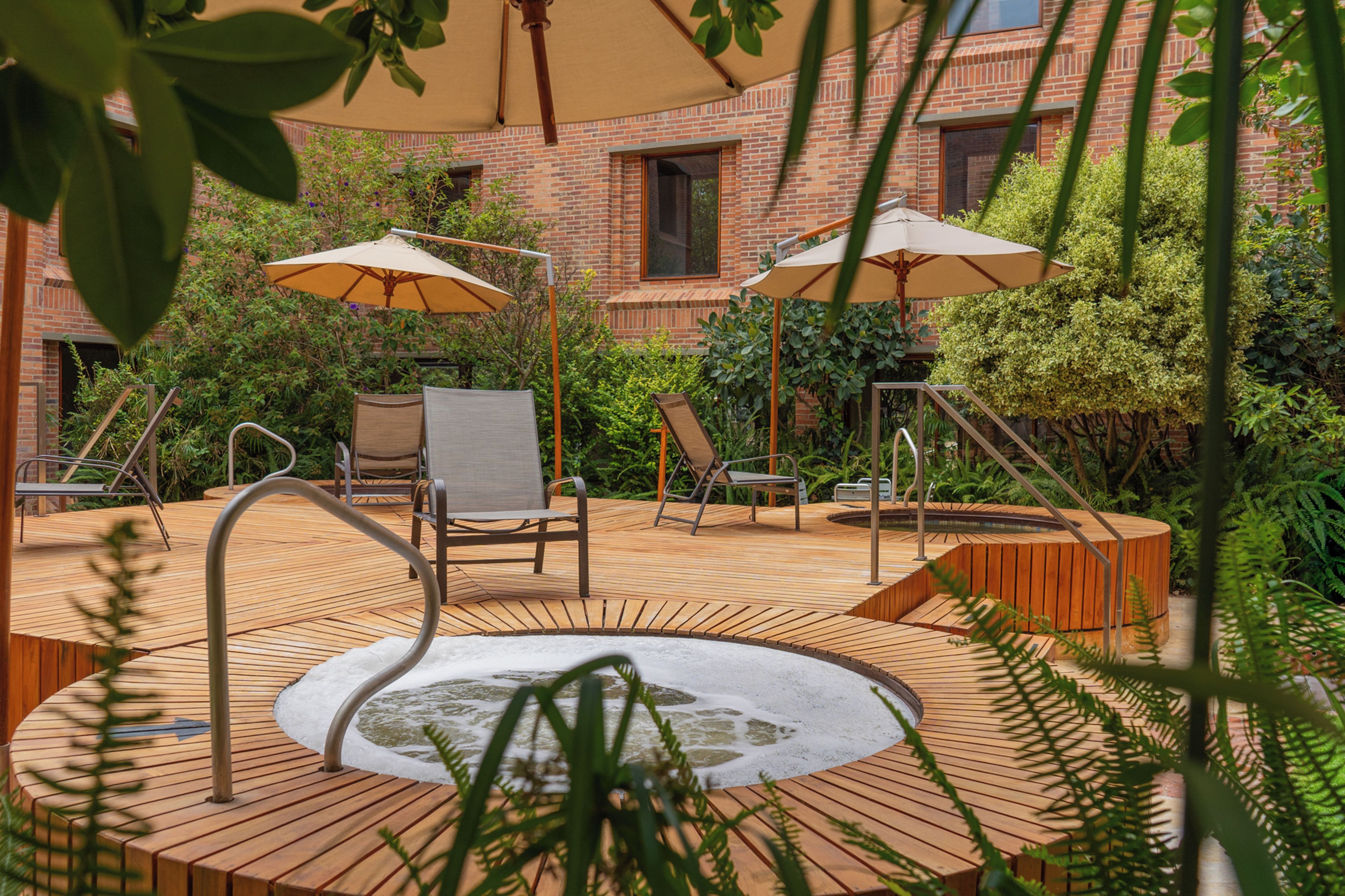 A wooden deck with a hot tub, two lounge chairs, and two umbrellas.