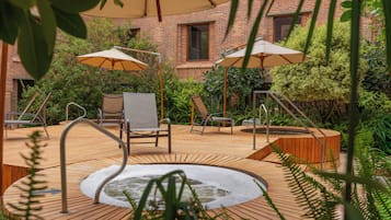 A wooden deck with a hot tub, two lounge chairs, and two umbrellas.